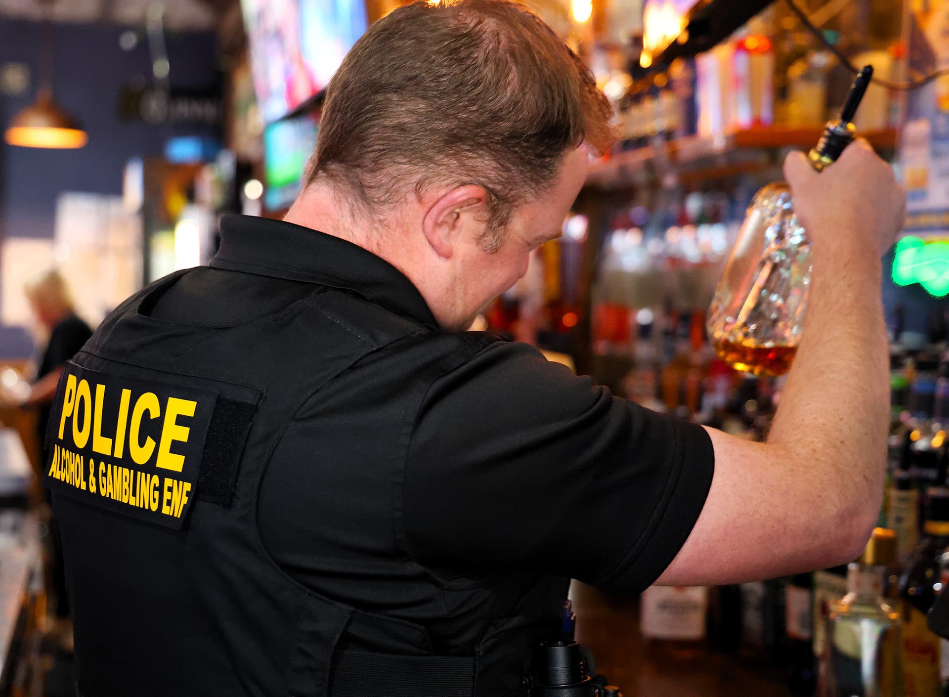An alcohol and gambling agent is inspecting a liquor bottle at a bar.