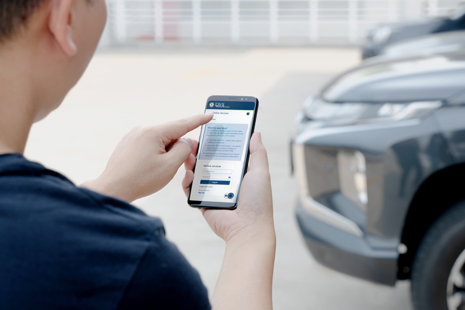 Picture showing man standing near a car and holding a smart phone with the MyDVS login screen on it.