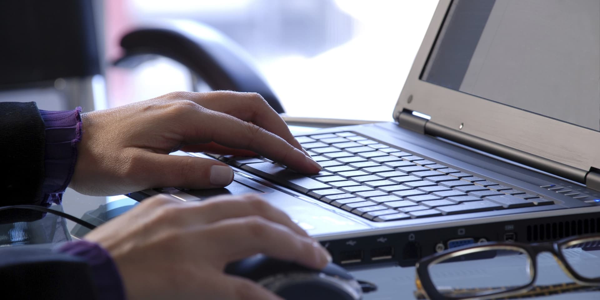 Close up of hands working on a laptop with a pair of glasses in the foreground