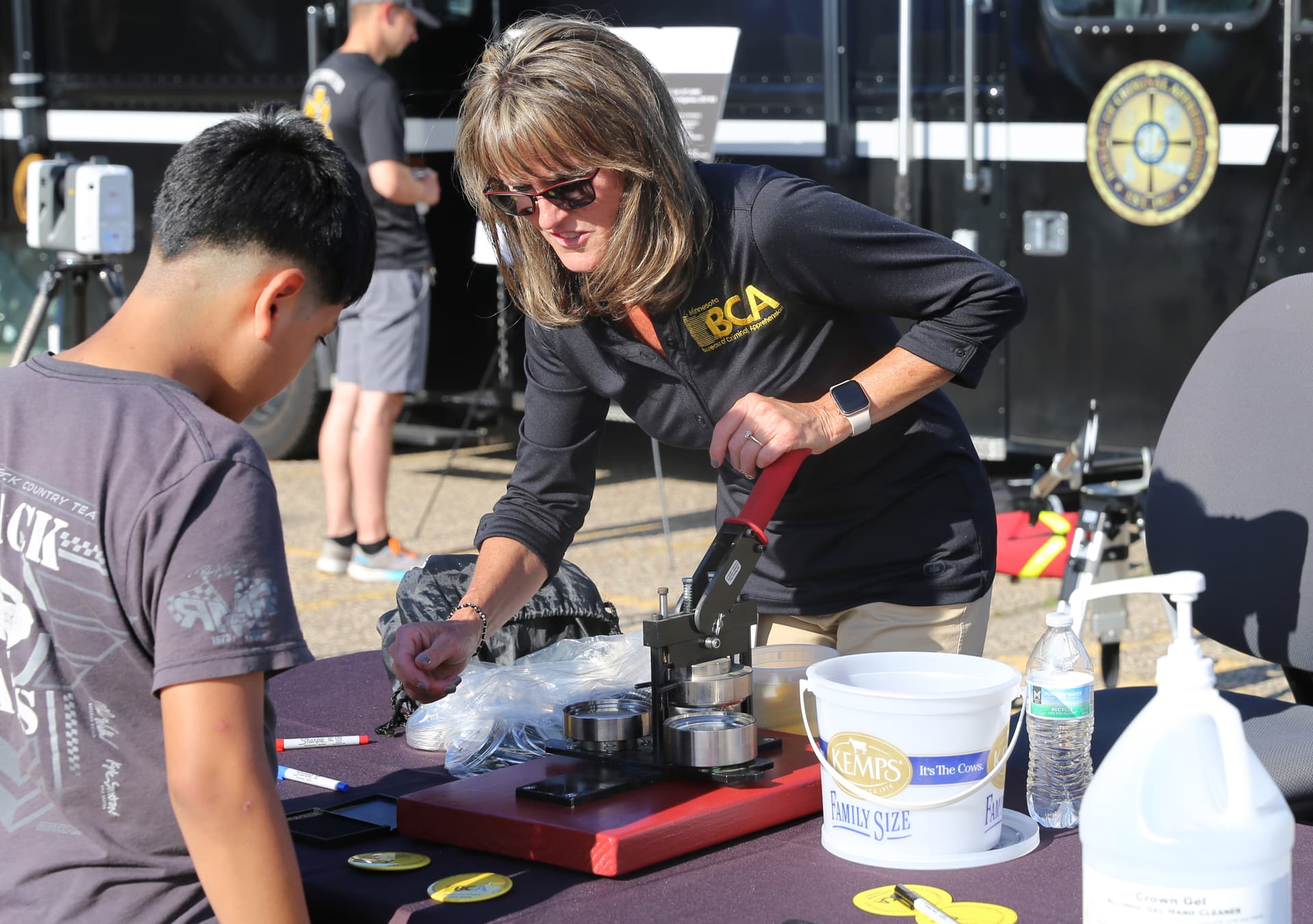 A Bureau of Criminal Apprehension staff member talks with kids at a table at an event. 