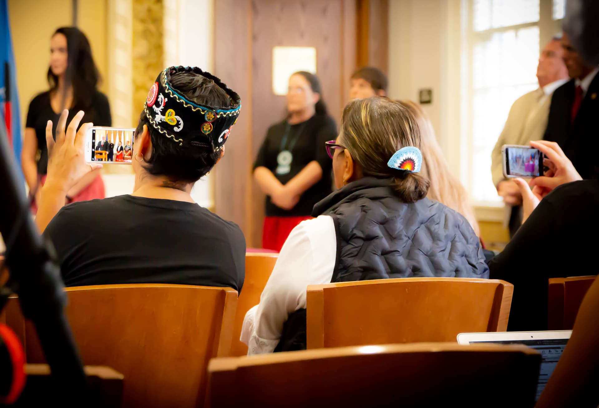 People in the crowd take photos of a meeting of the Missing and Murdered Indigenous Relatives Task Force