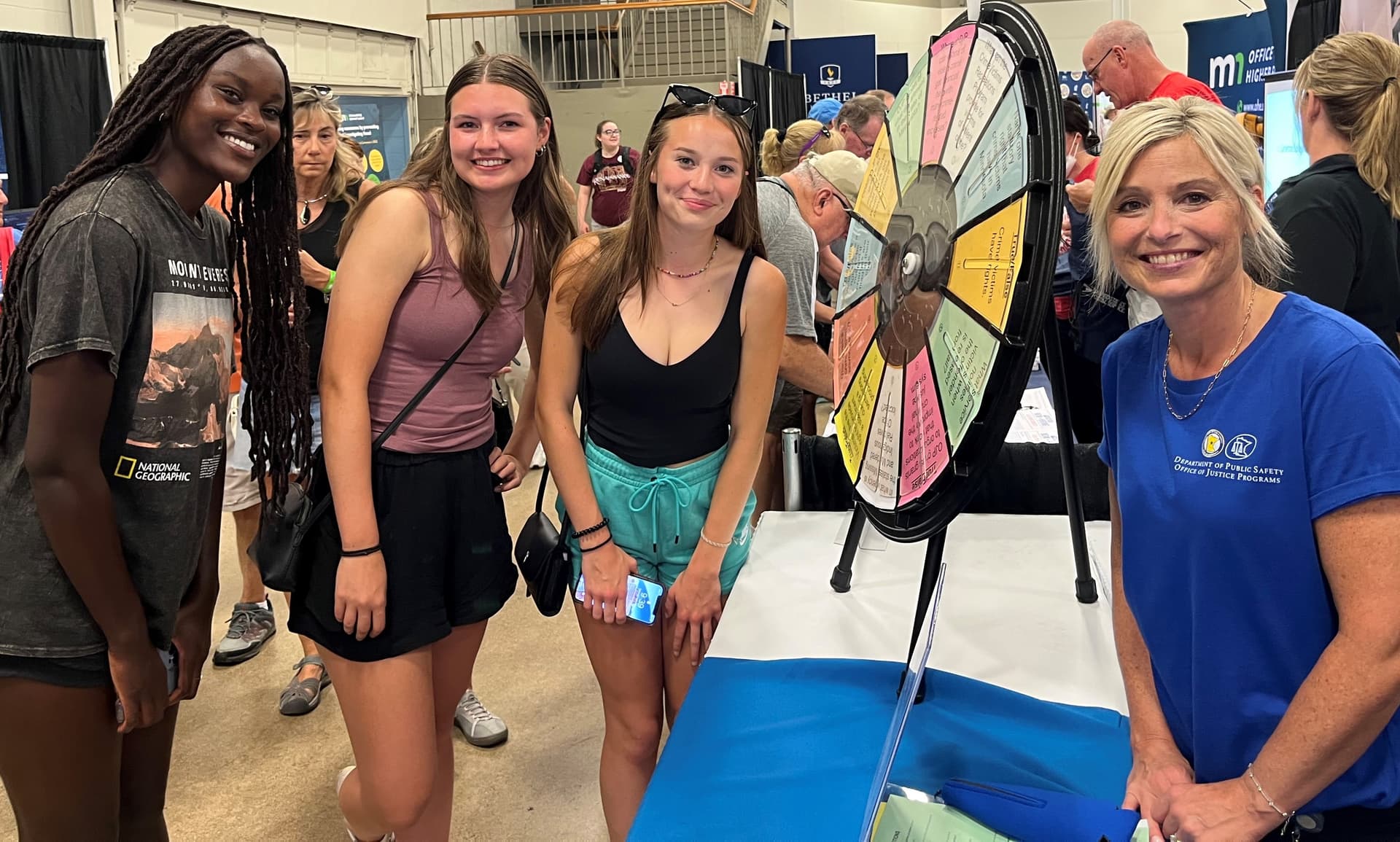 A staff member stands at a State Fair booth with three other people.