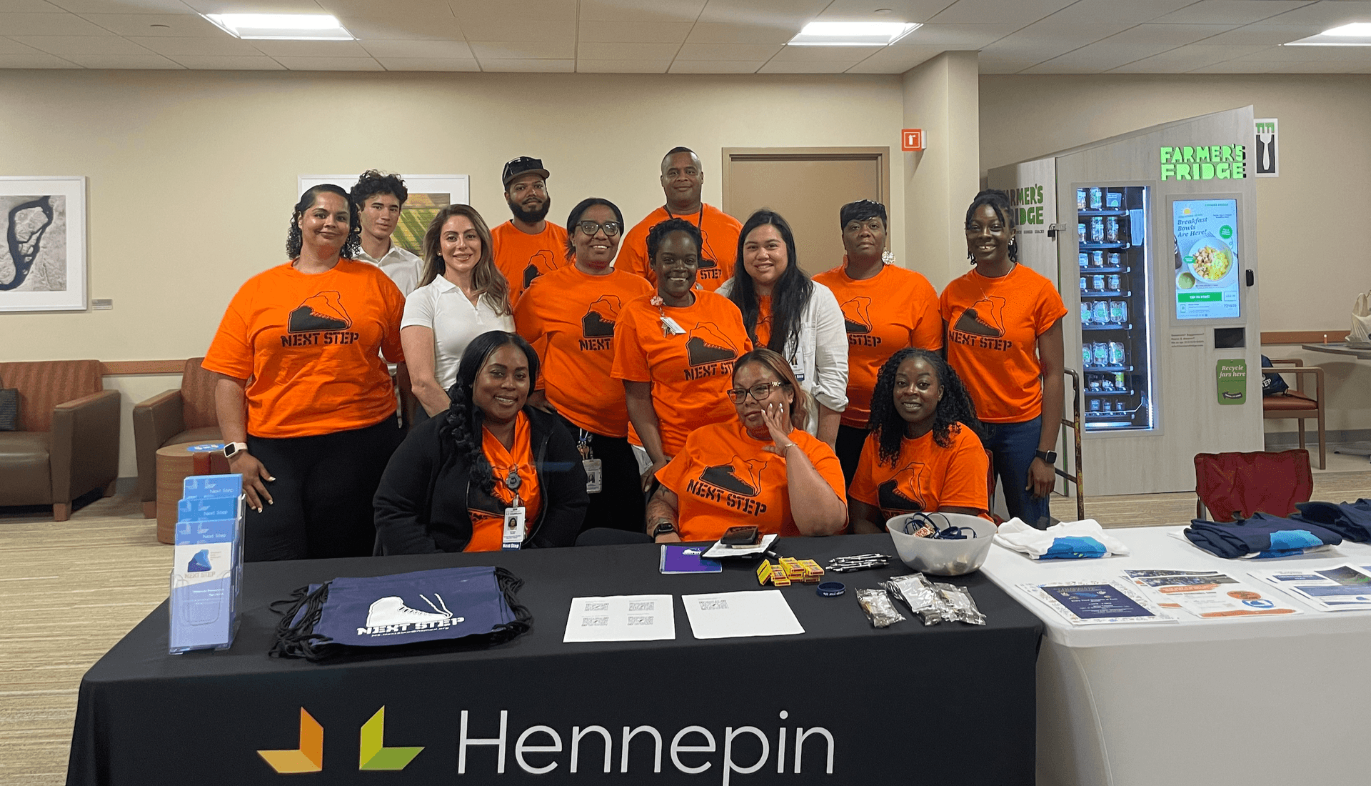 People in orange Next Step shirts standing behind a table with swag.