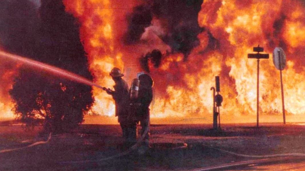 Firefighters work in front of a wall of flame