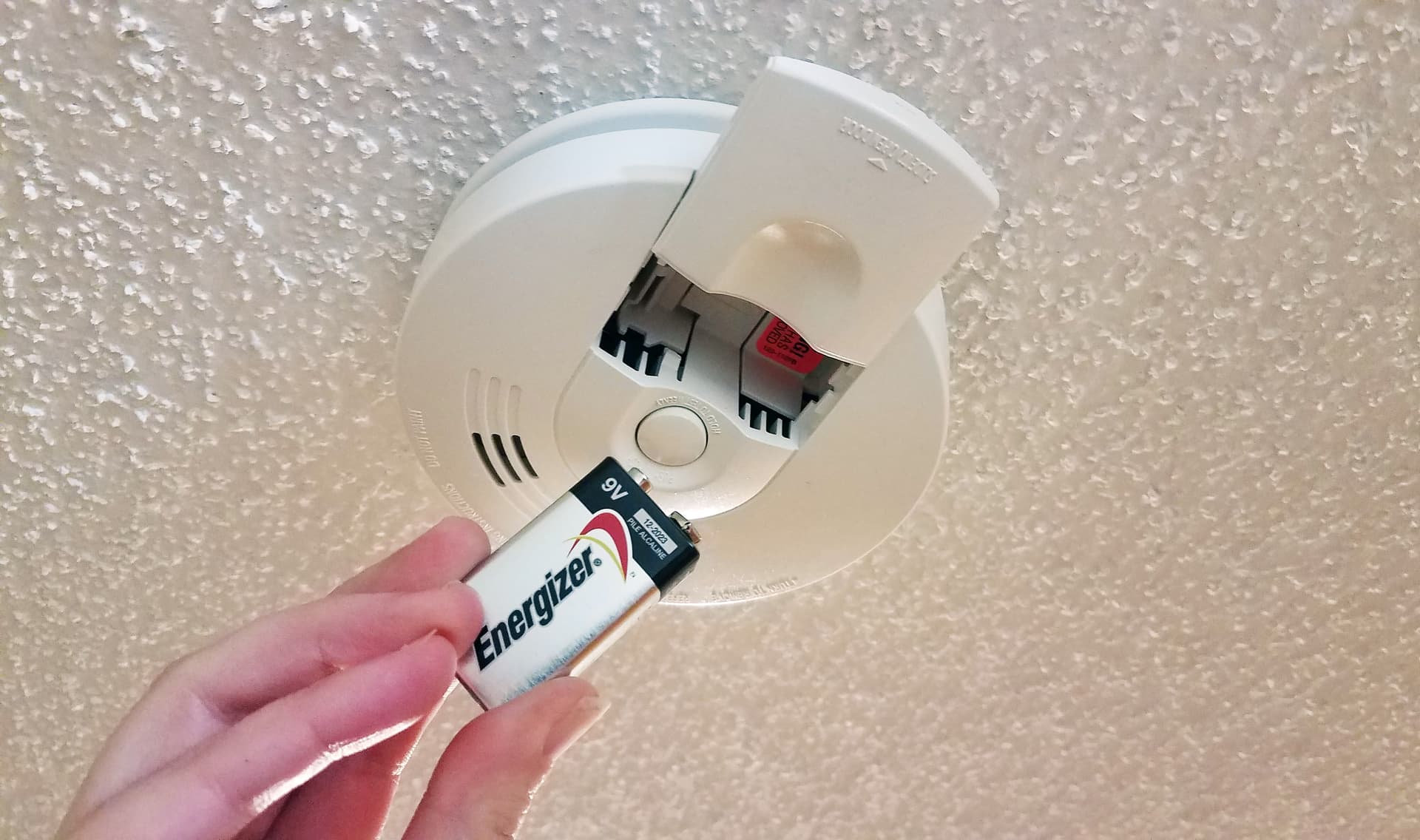 Someone putting a battery in a smoke alarm. 