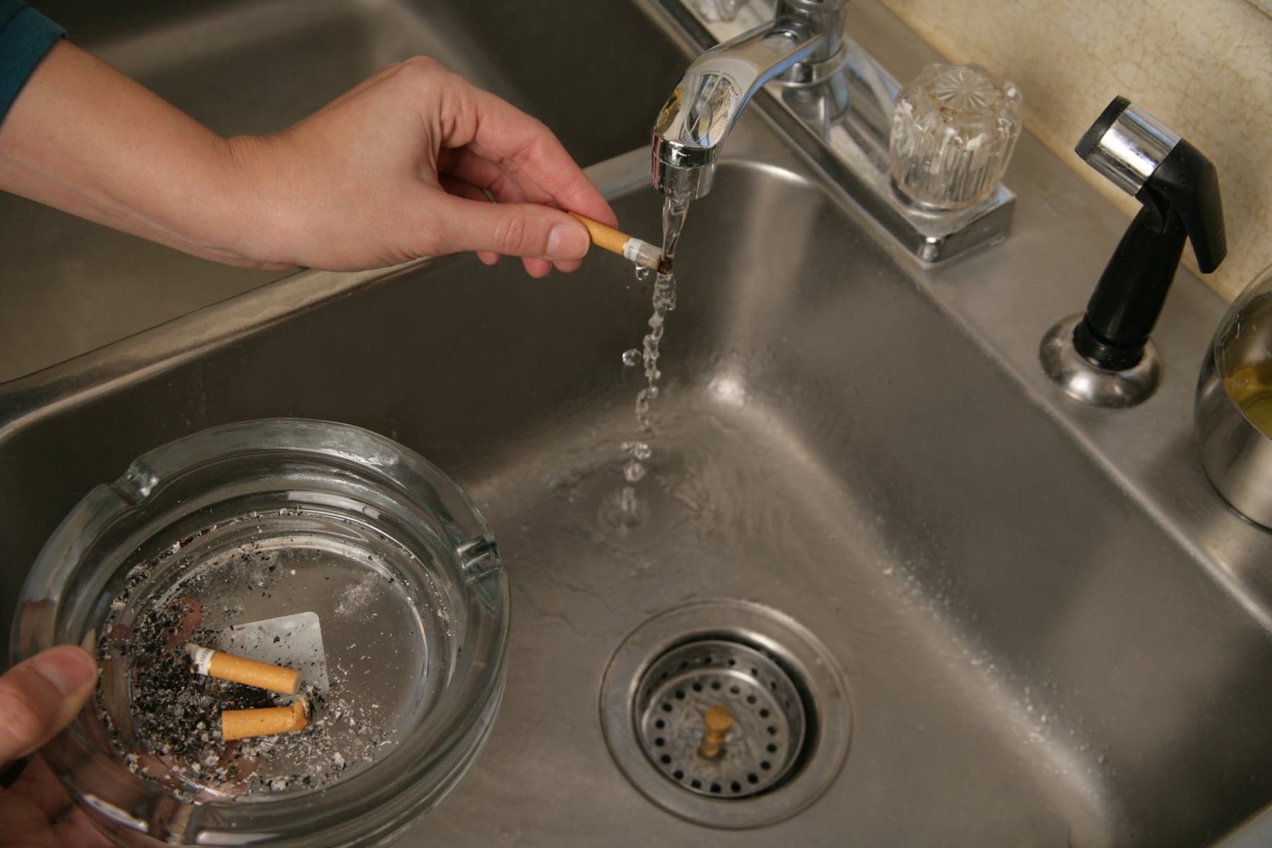 A woman runs a cigarette under water to put it out. 